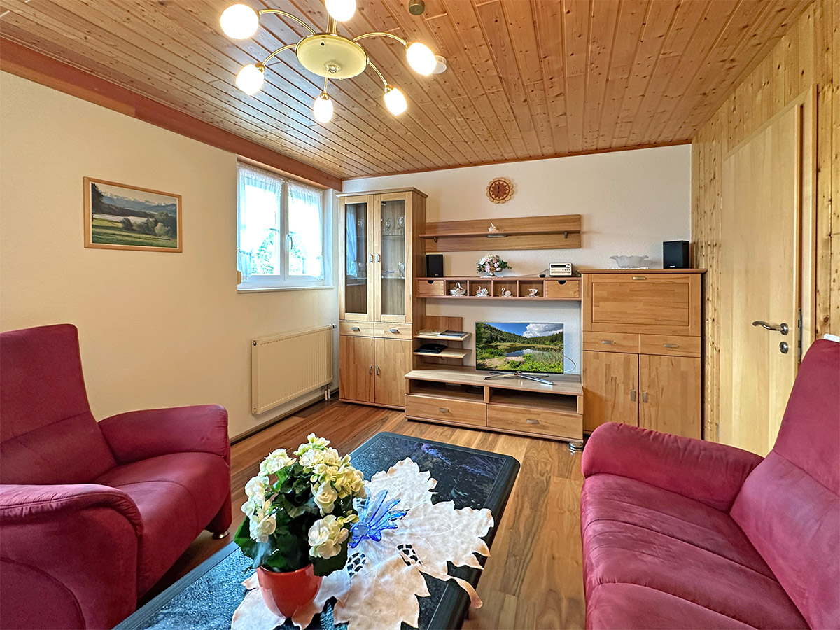 Gemütliches Wohnzimmer der Ferienwohnung Zwei Linden – warme Holzdecke und rote Sitzgruppe